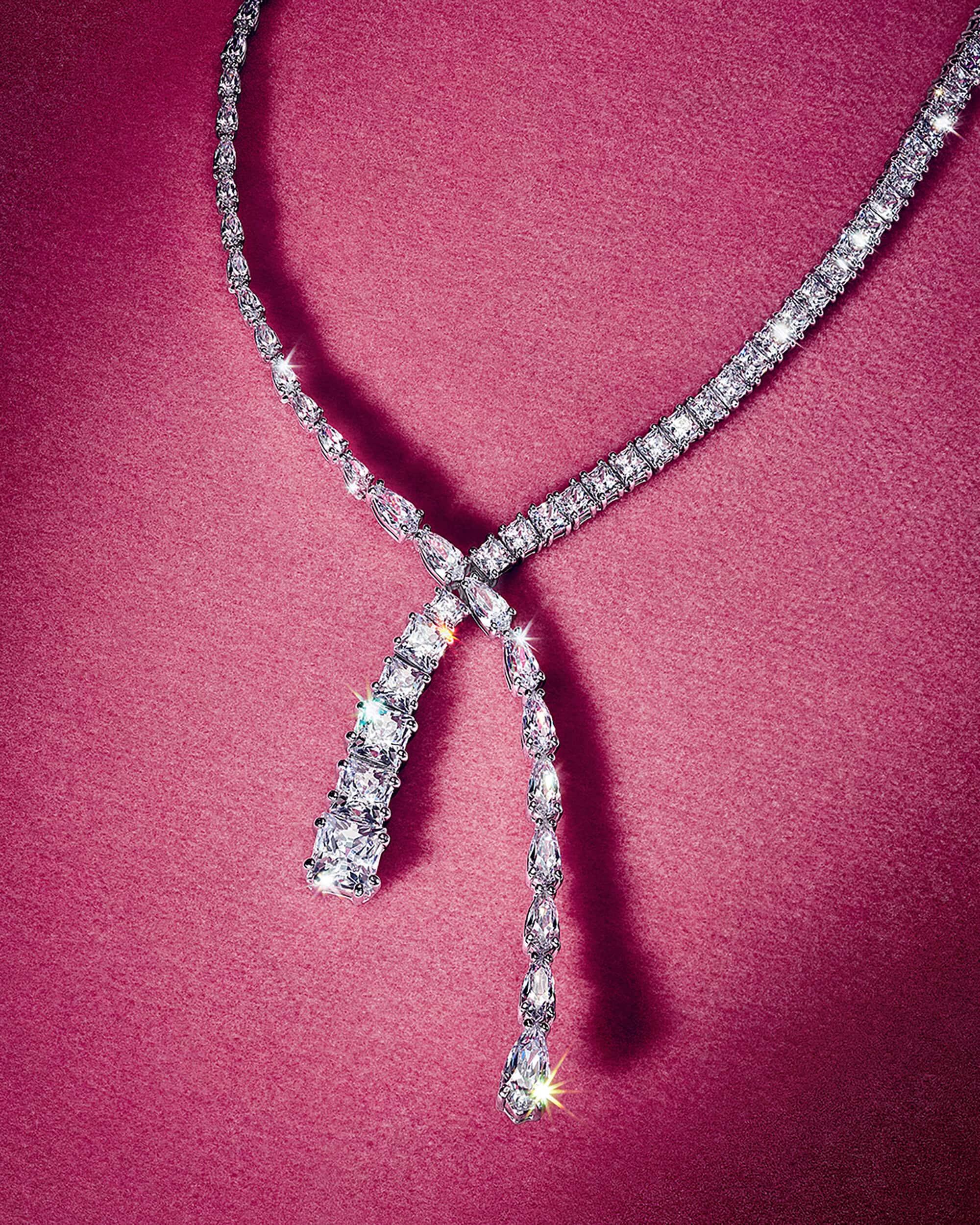 Sparkling crystal tennis necklace draped against a deep pink textured fabric background.