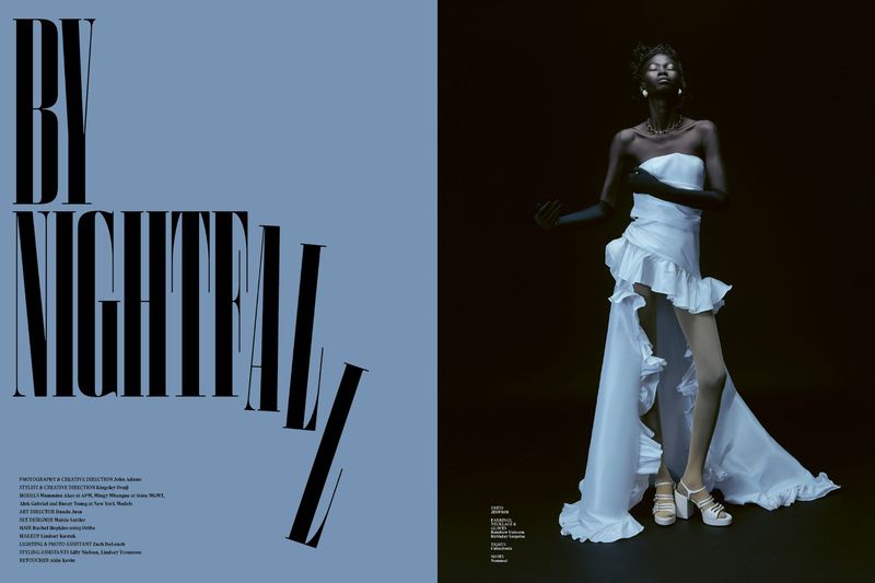 Editorial fashion shot: a Black fashion model poses in a white gown on a dark background, complemented by 'BY NIGHTFALL' text on left.