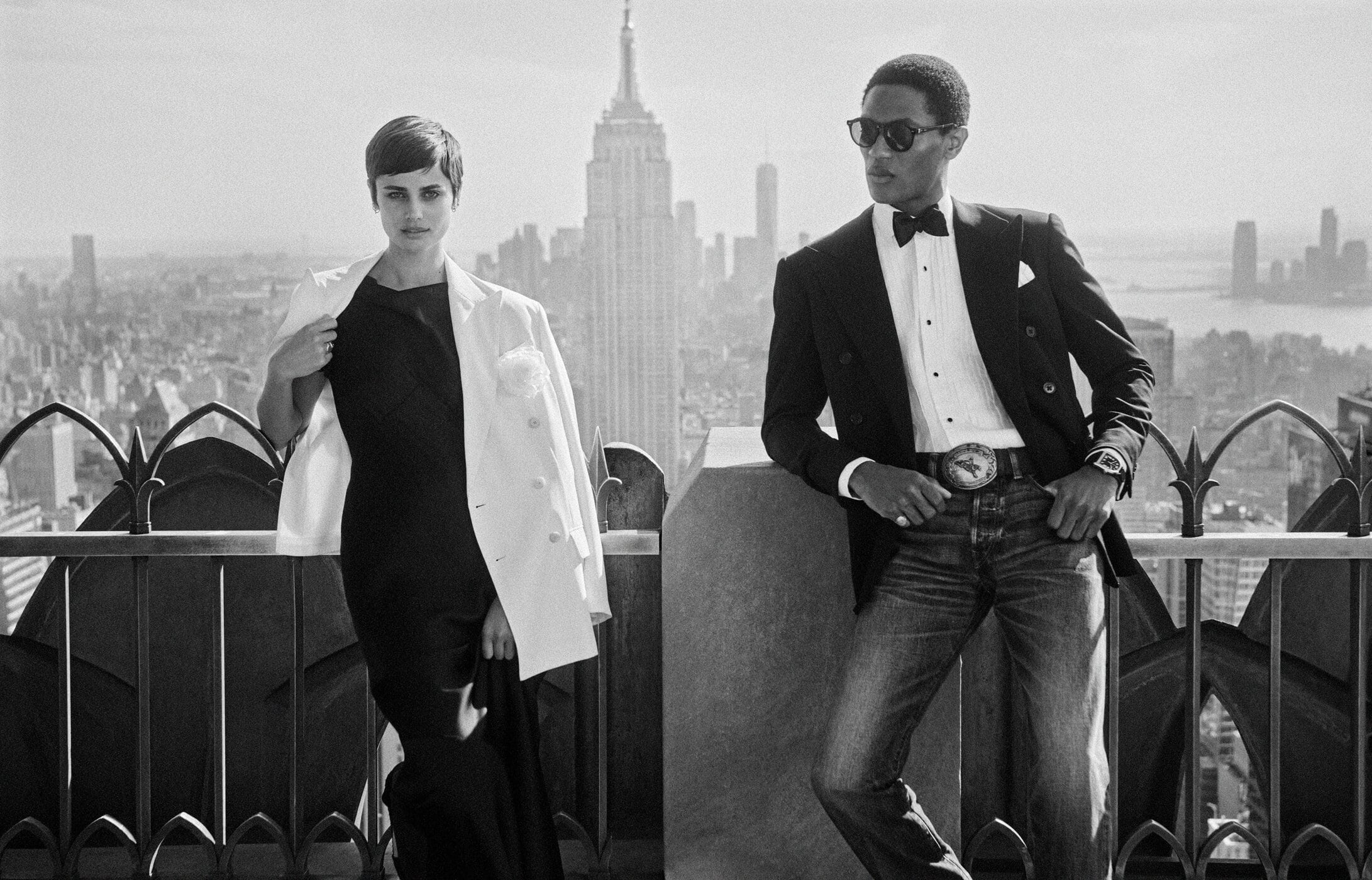Black and white portrait of a woman and a man posing on a rooftop with the New York City skyline in the background.