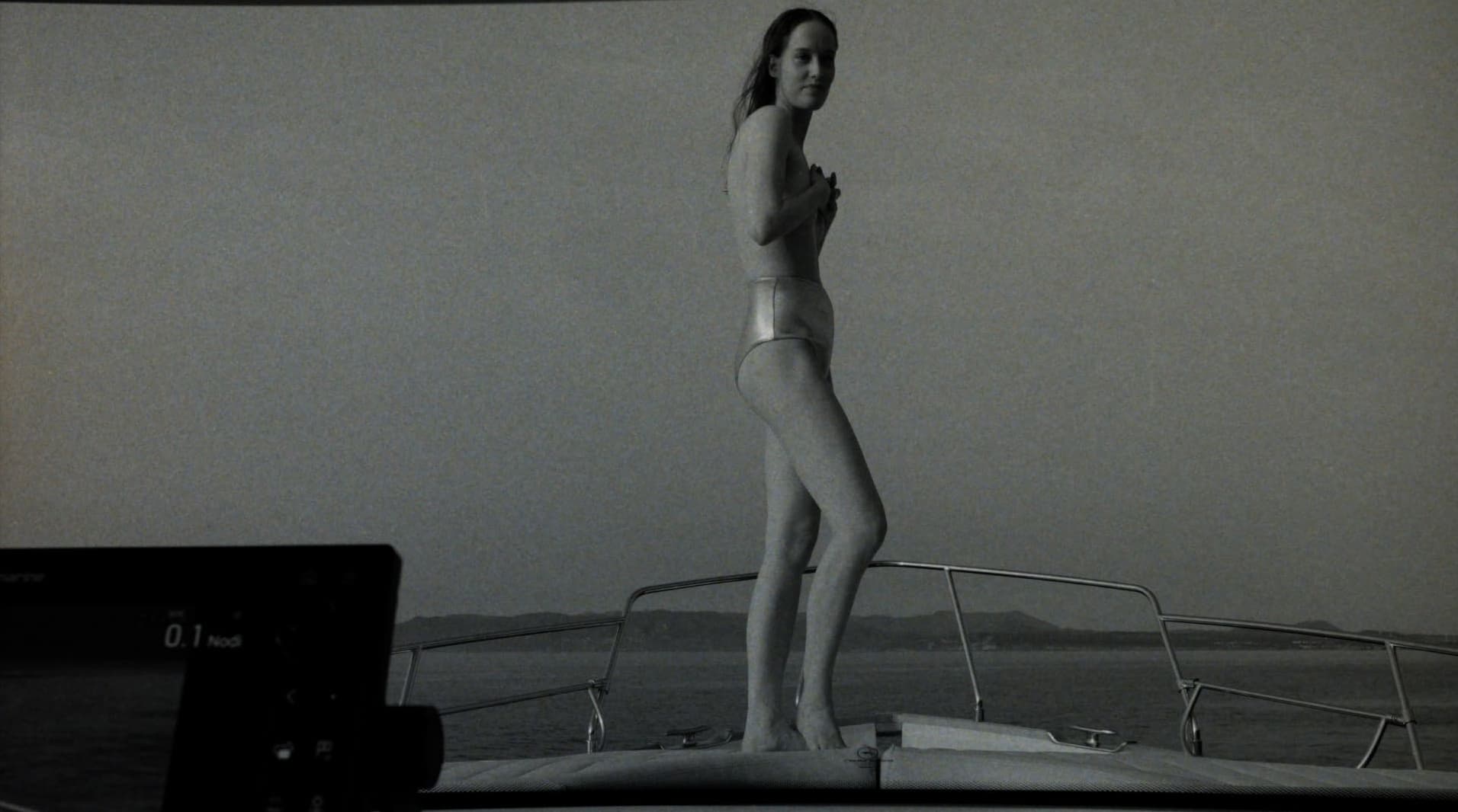 Model standing on a boat deck against an open water horizon in a black and white campaign image for Adriana Degreas.