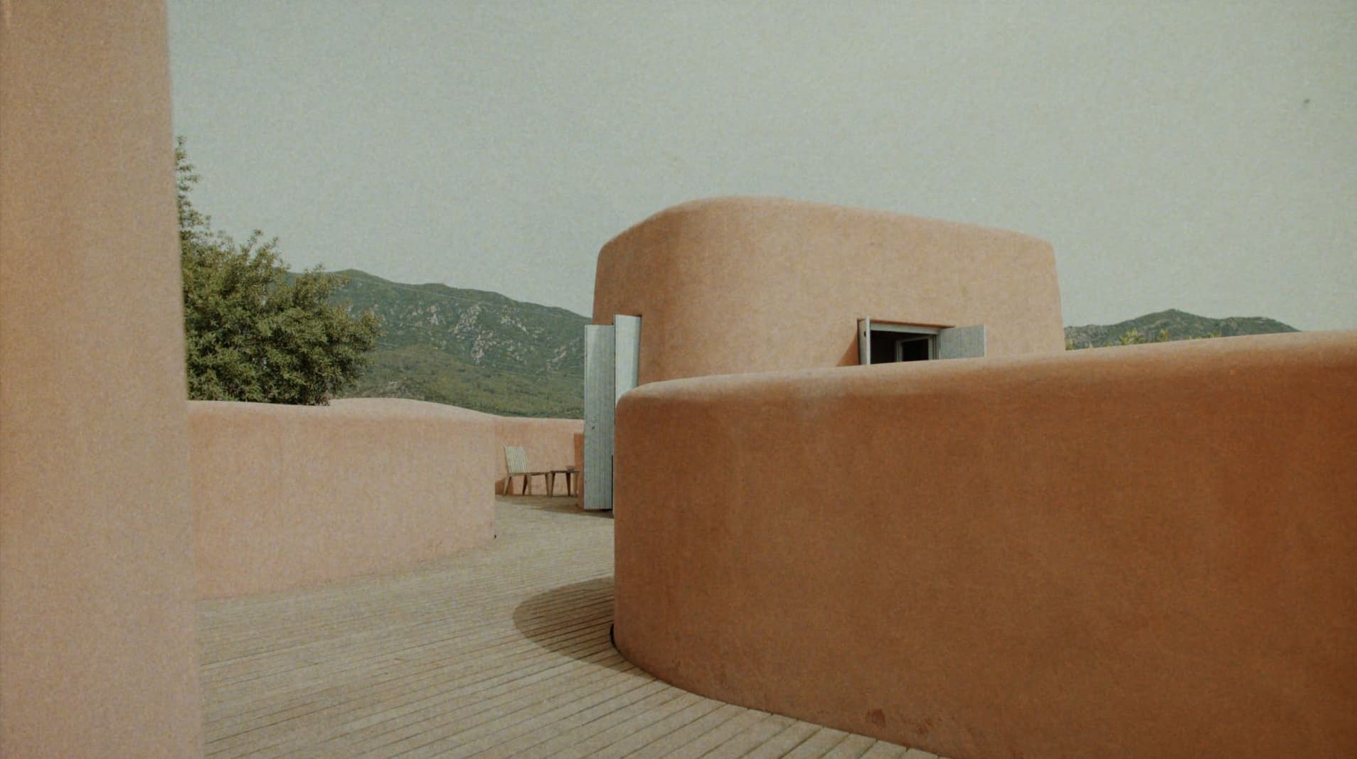 Curved terracotta walls and wooden decking under an overcast sky for Adriana Degreas Spring 2025 campaign.
