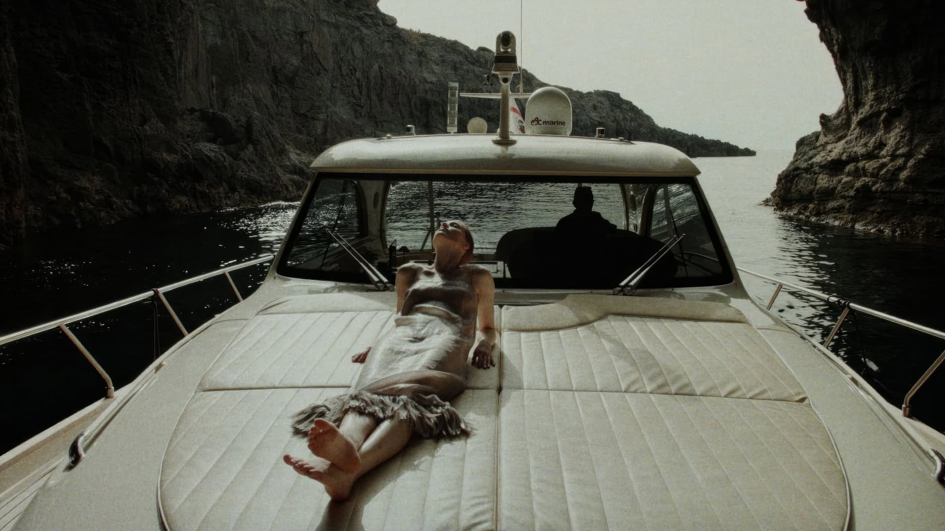 Model lying on the deck of a yacht moored in a coastal cave setting for Adriana Degreas Spring 2025 campaign.