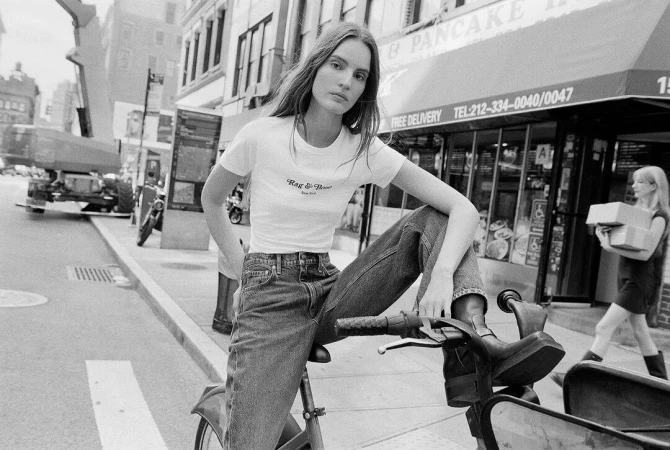 Model seated on a bicycle in the street wearing a white t-shirt and denim jeans for Rag and Bone.