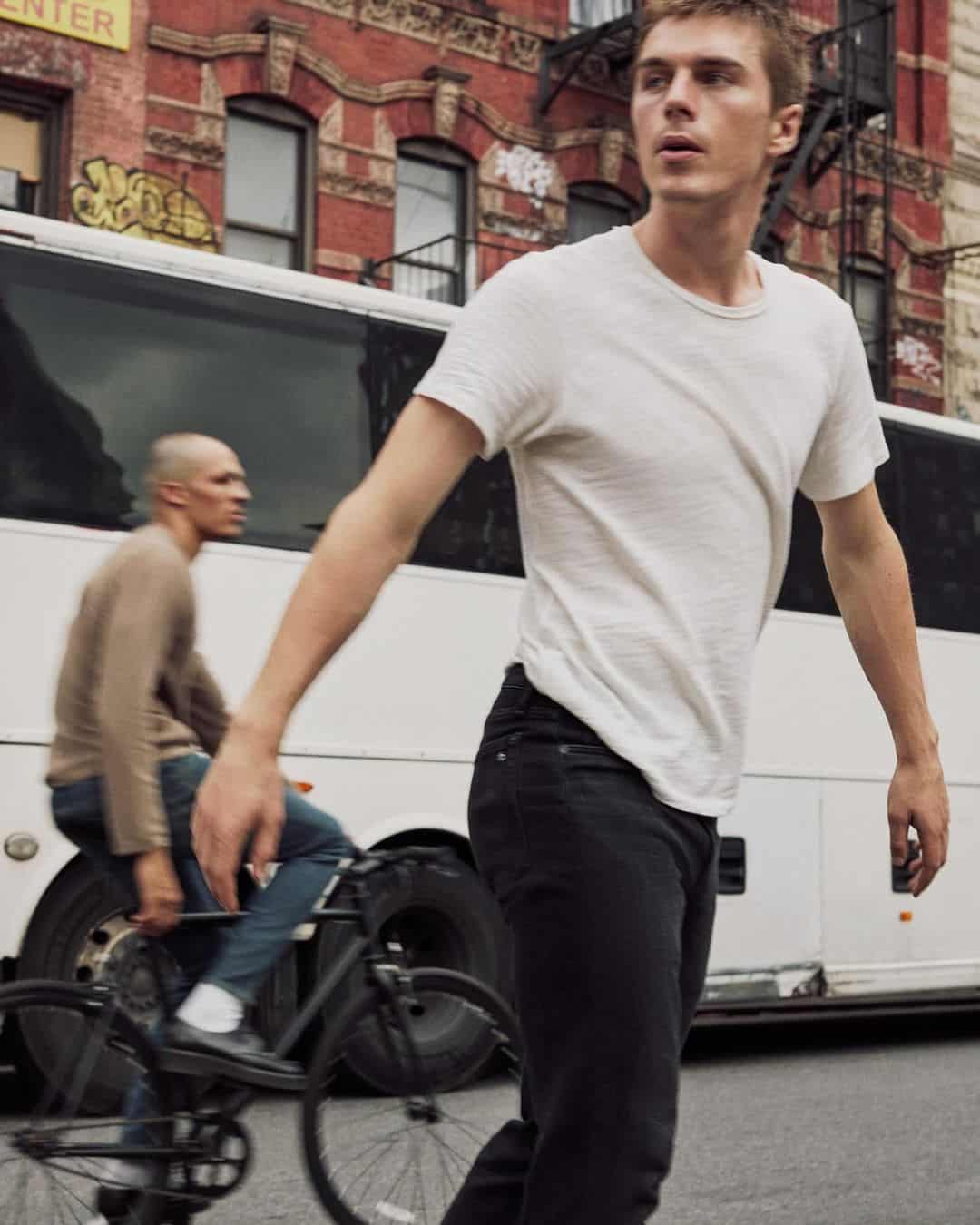 Man wearing a white t-shirt walking past a white bus and brick building
