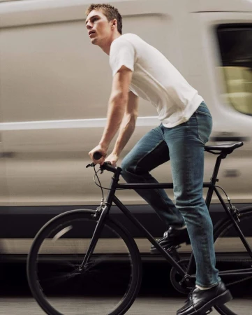 Man riding a black bicycle in front of a moving white van wearing a white t-shirt and blue jeans