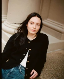 Model Tilda Lindstam wearing a black cardigan and blue jeans leaning against architectural columns