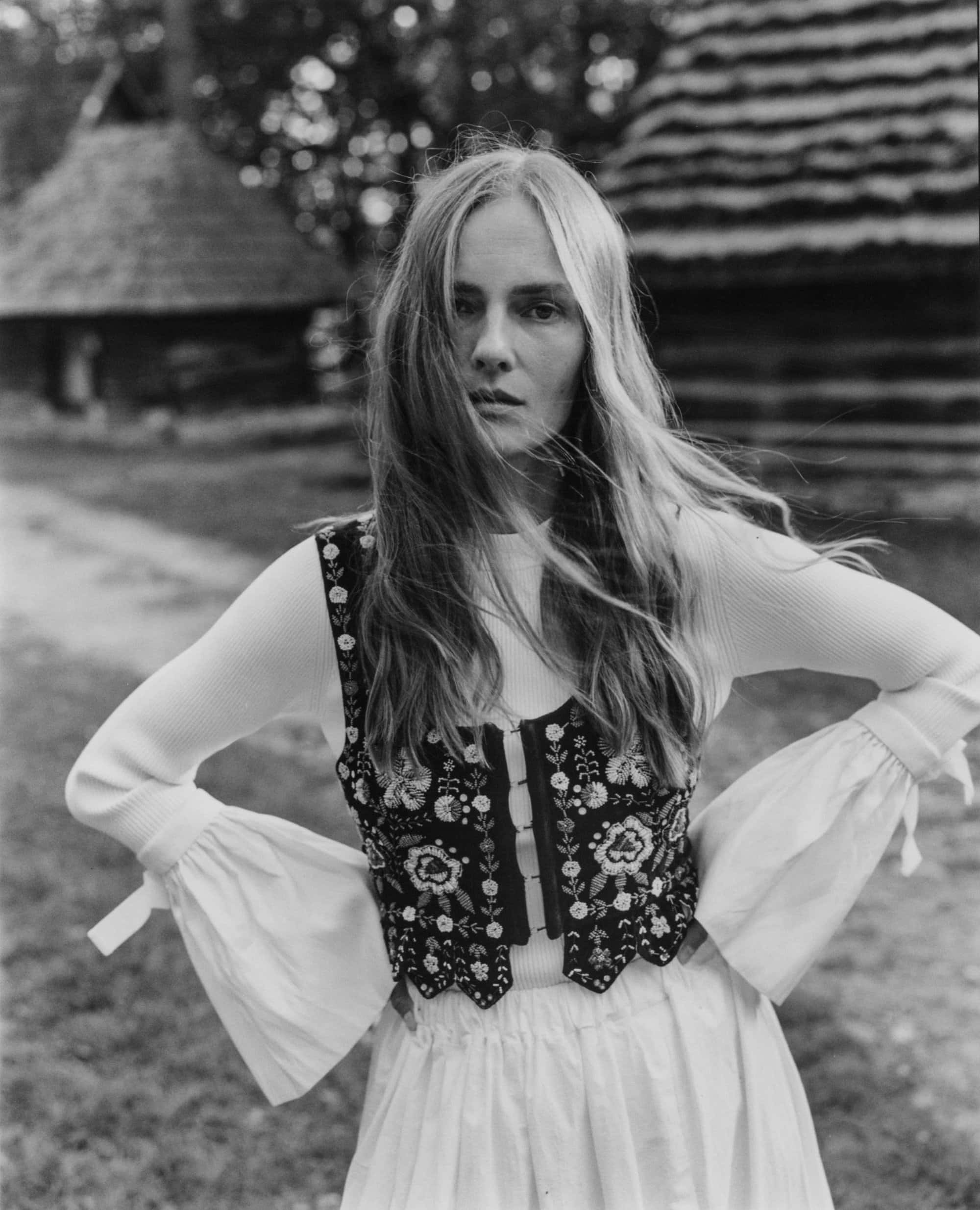 Monochrome portrait of a woman standing outdoors wearing an embroidered vest and white blouse with ruffled sleeves