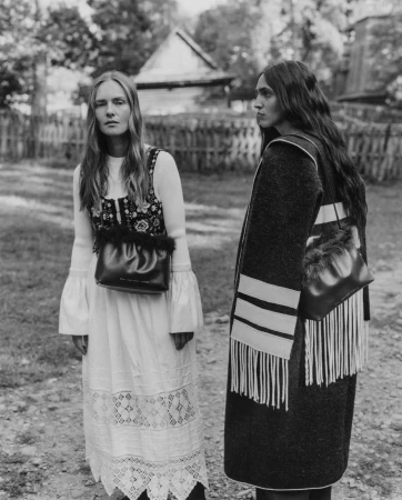 Two female models posing outdoors wearing Chylak handbags against a rustic rural background in a black and white campaign image.