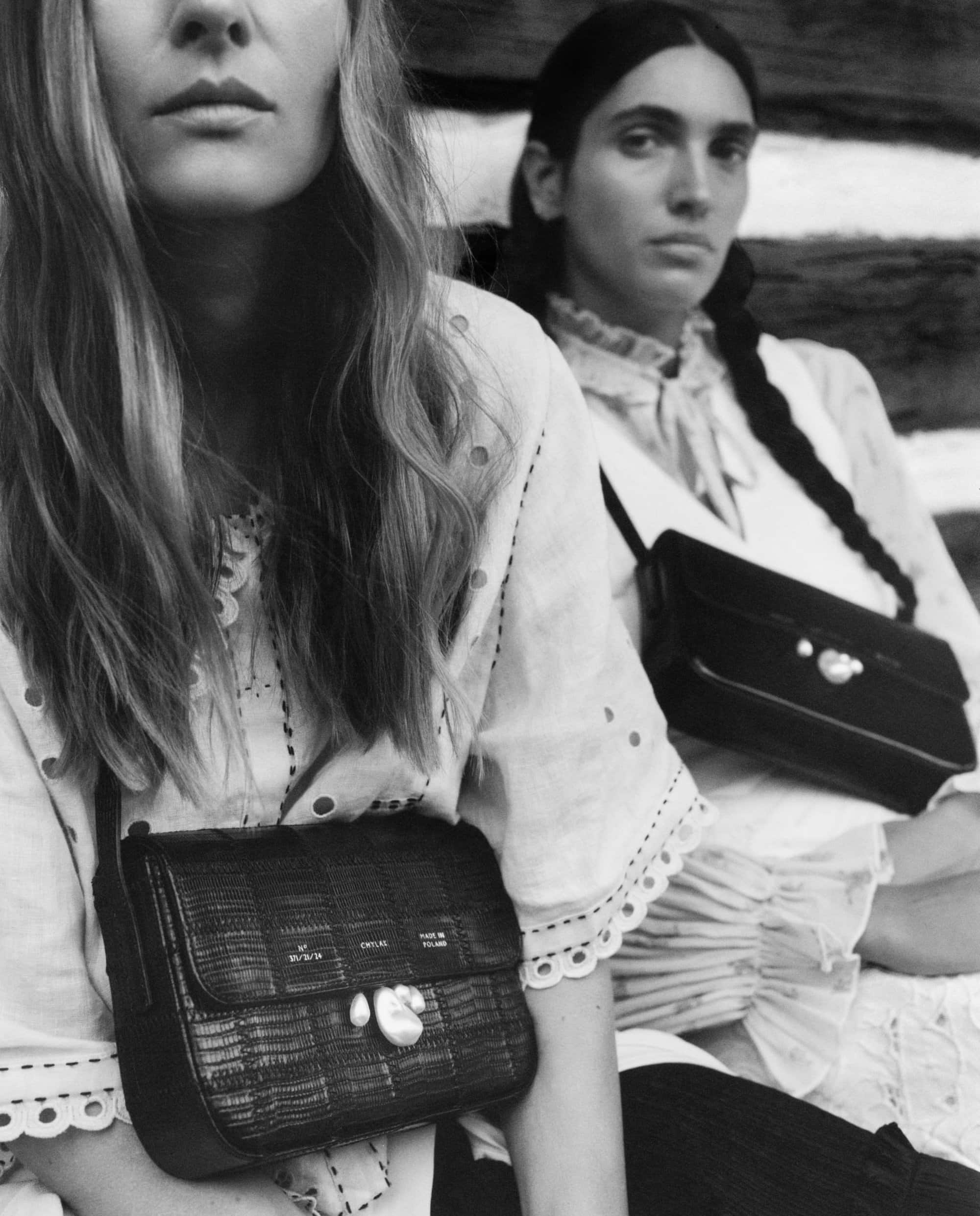 Black and white portrait of two women wearing white blouses and holding textured black leather shoulder bags with pearl closures for Chylak