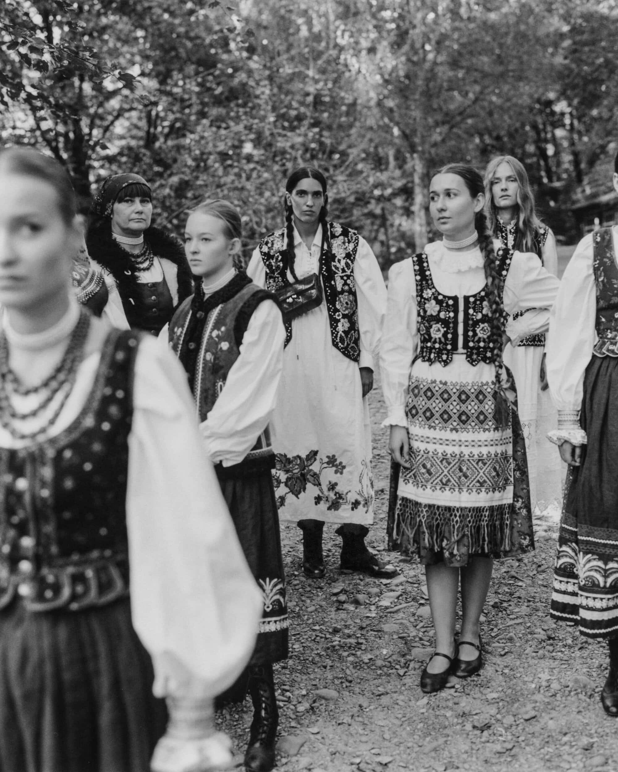 Monochrome fashion campaign image by Chylak featuring a group of women in embroidered traditional vests and skirts outdoors.