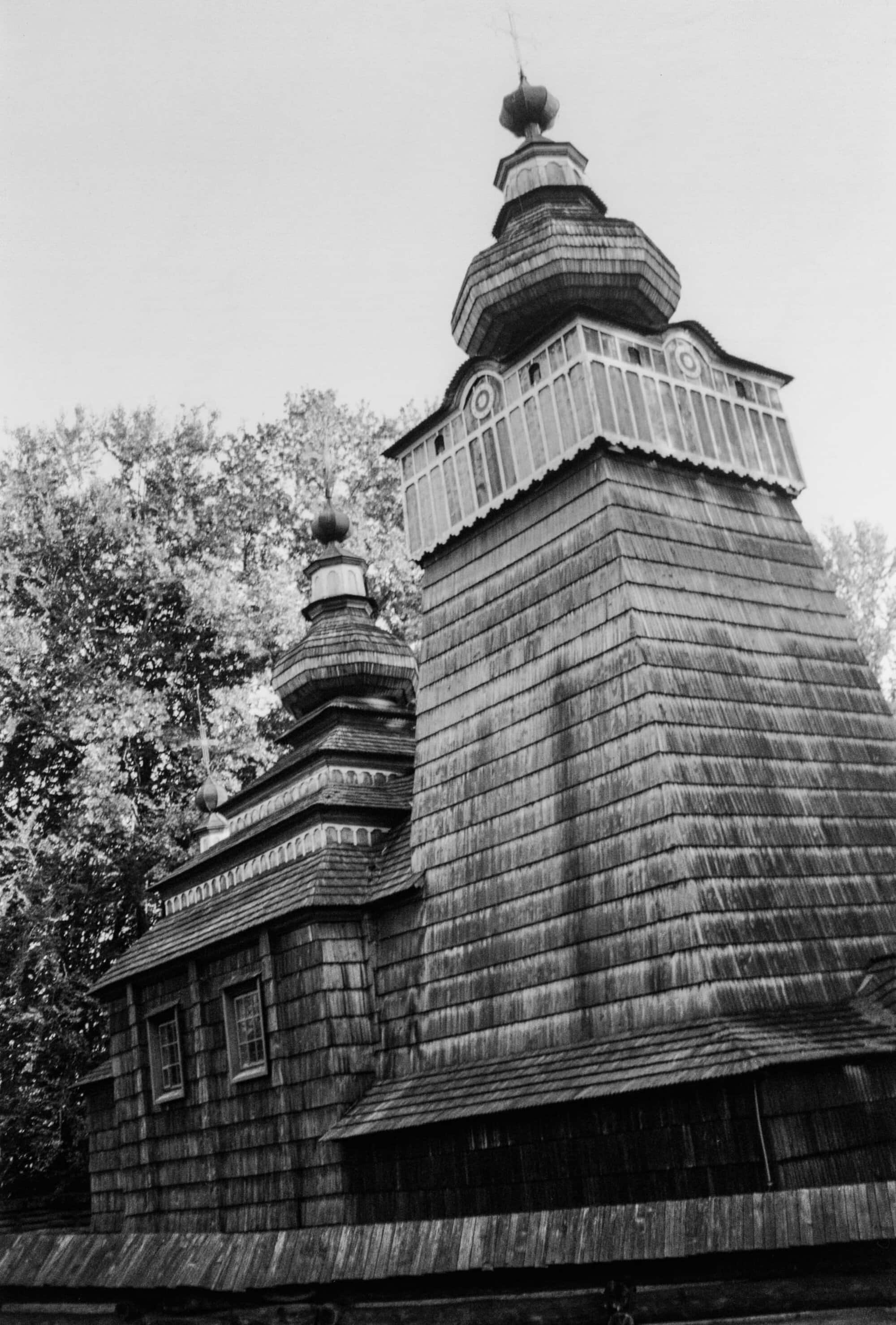 Monochrome architectural photograph of a traditional wooden church with tiered cupolas under an overcast sky.