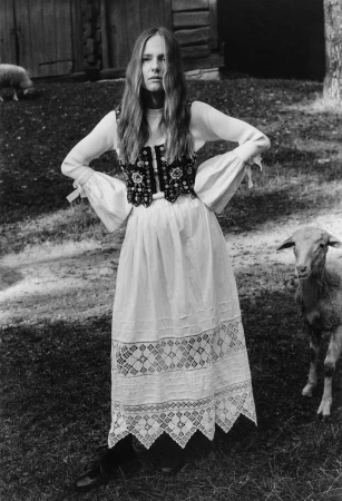 Black and white portrait of a woman standing outdoors with sheep wearing an embroidered vest and long dress for Chylak.