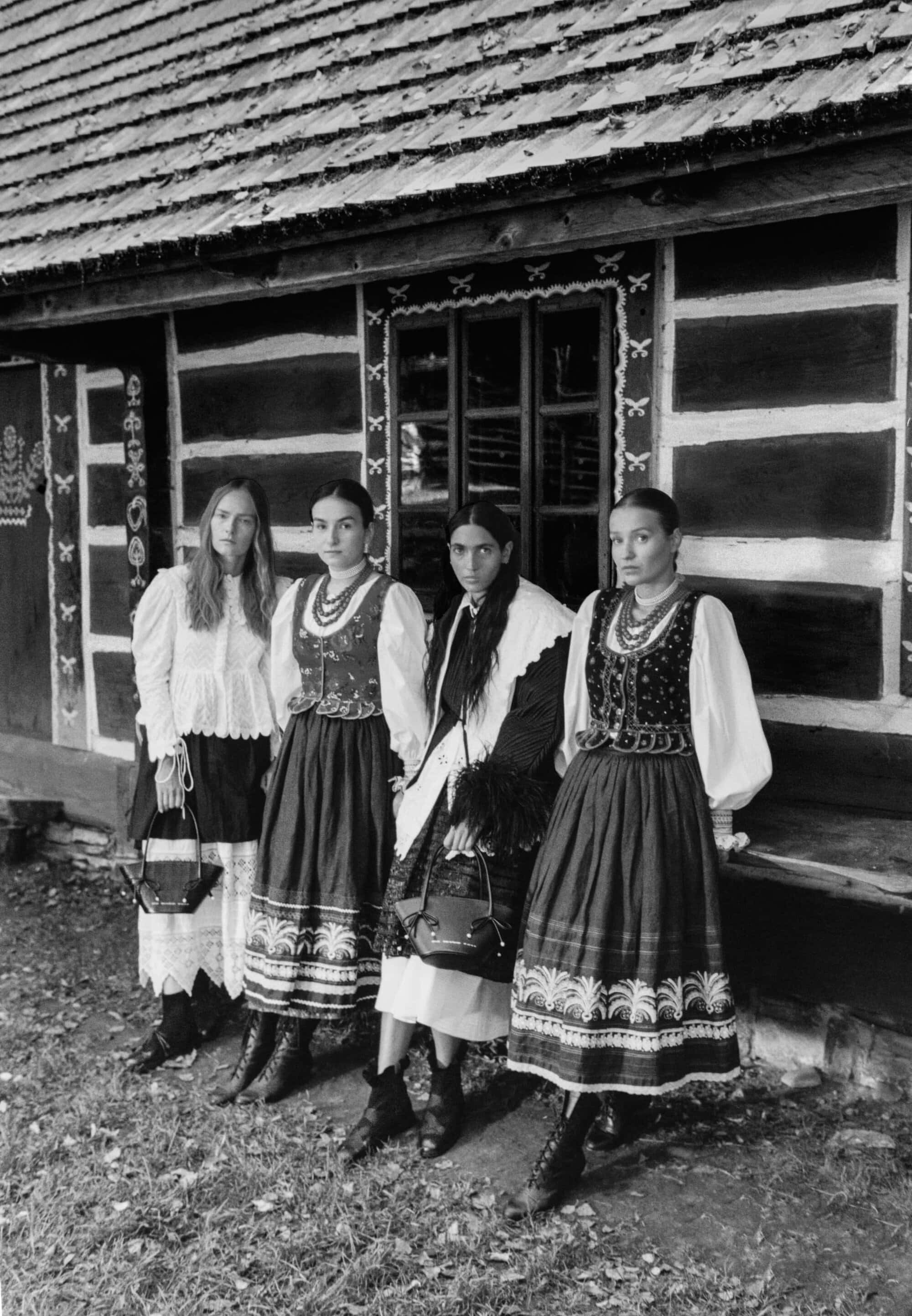 Four models in traditional folk-inspired apparel standing outside a dark wooden cabin for the Chylak Fall 2024 campaign.