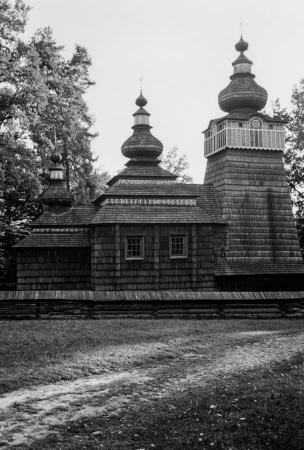 Black and white photograph of a traditional wooden church with tiered onion domes and shingled roof, surrounded by trees.
