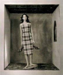 Model wearing a plaid dress and holding heels standing inside a structured set for Acne Paper project Lux Et Tenebrae