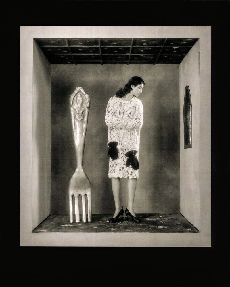 Model standing inside a small room set alongside a giant fork sculpture, wearing lace attire.