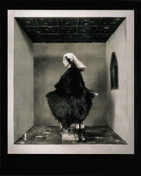Model Raya Martigny in a textured black feathered dress and head covering inside a set-designed diorama room by Acne Paper.