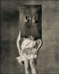 Model wearing a textured fringed dress with head covered by a dark sculptural mask for Acne Paper project Lux Et Tenebrae