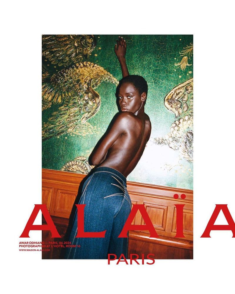 Model Awar Odhiang in denim jeans posing against an ornate green and gold patterned wall for Alaïa