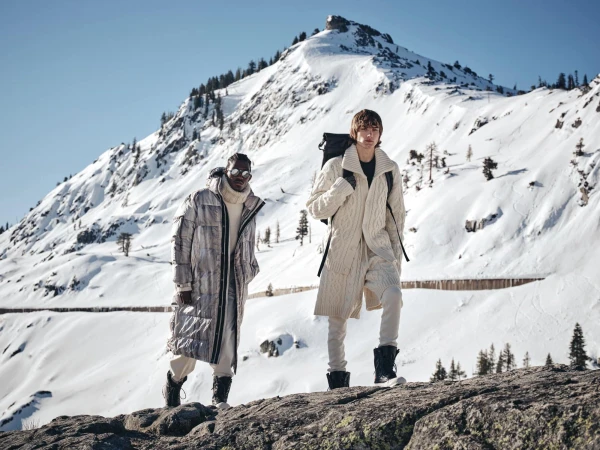 Two models standing on a snowy mountain ridge wearing winter outerwear for Todd Snyder x Woolrich Black Label campaign