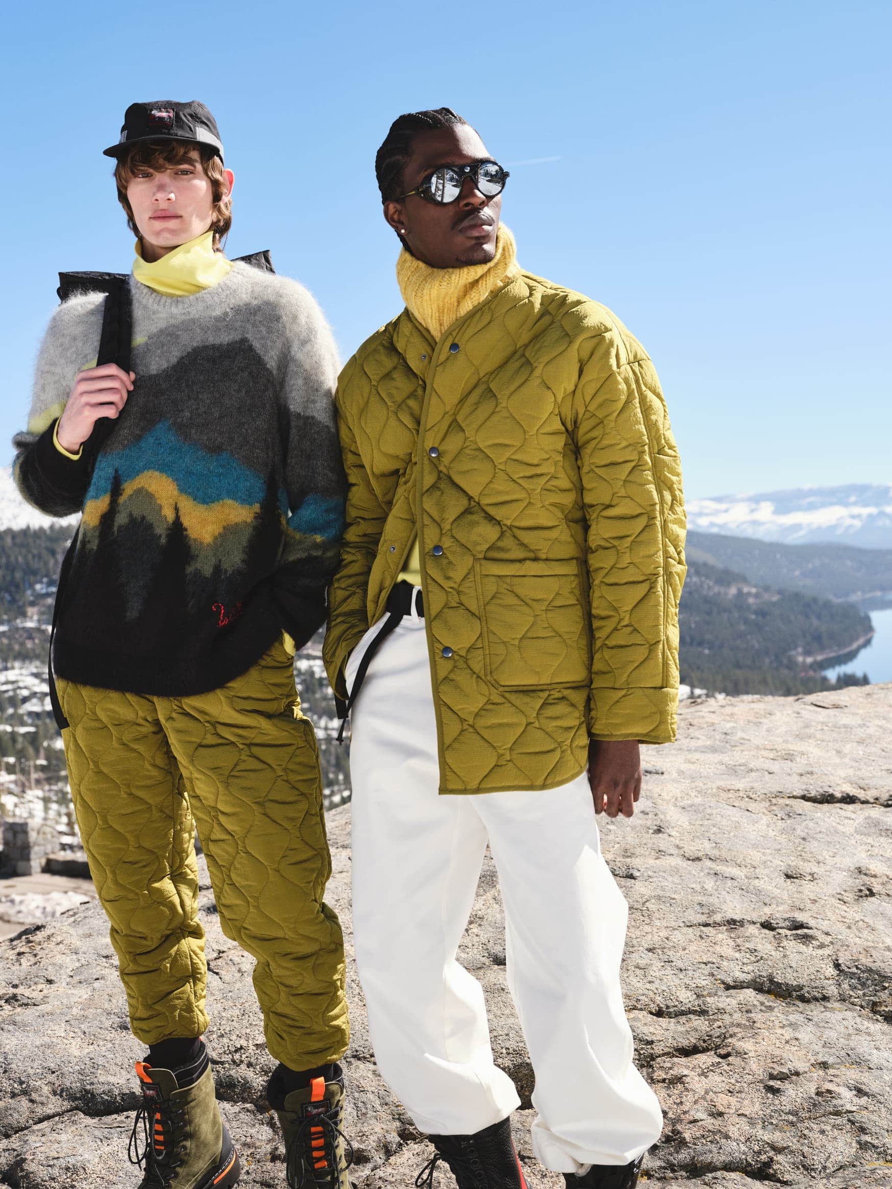 Two male models posing outdoors in winter apparel against a mountain lake backdrop, styled by Jim Moore and photographed by Kenny Thomas.