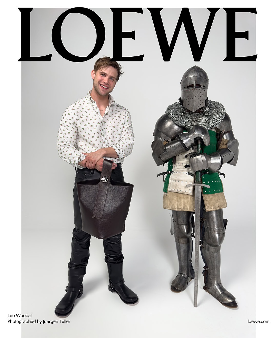 Man wearing patterned shirt and leather trousers holding a bucket bag next to a figure in full medieval armor