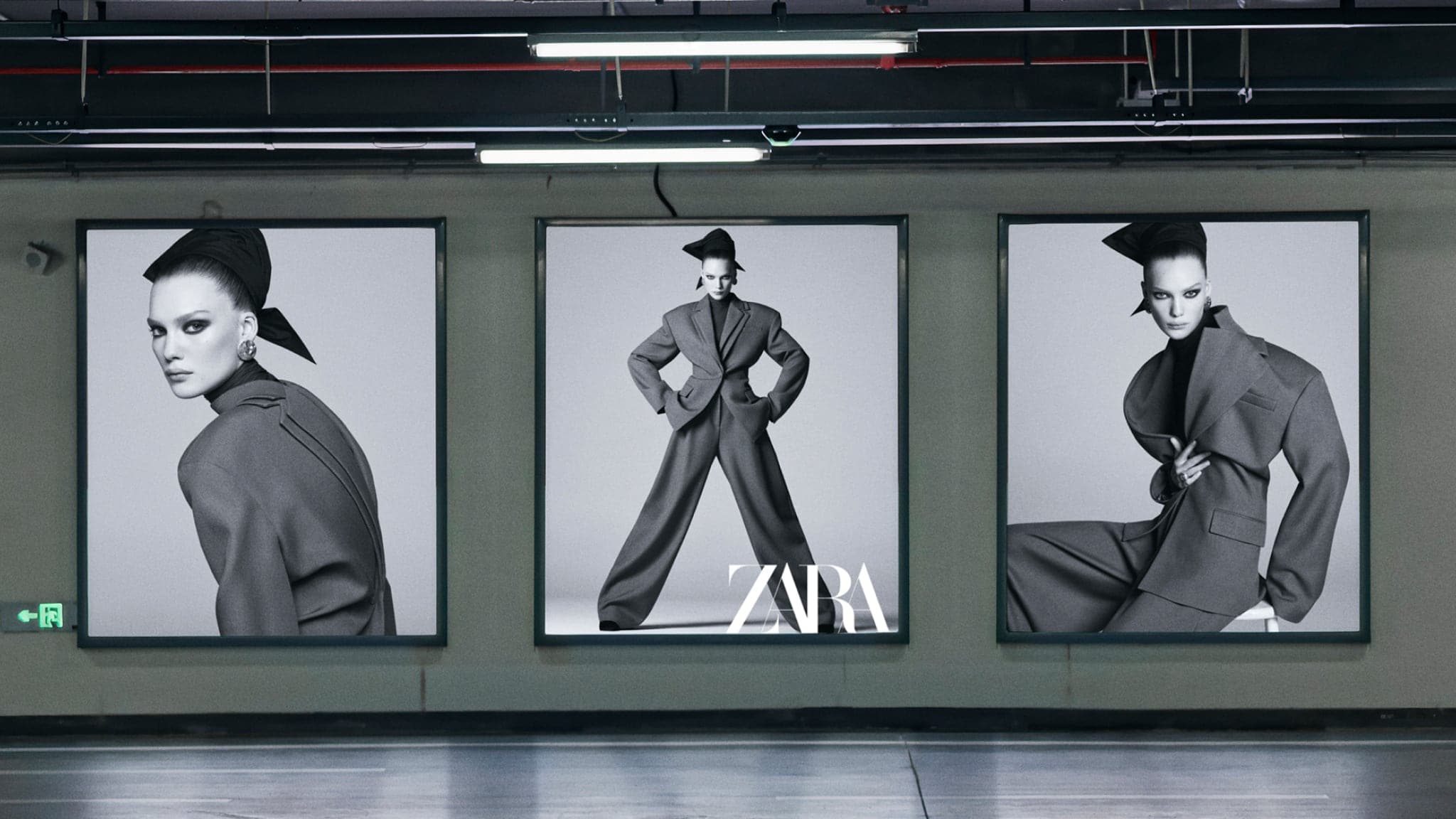 Three large backlit fashion billboard posters displaying a model in a tailored suit in a concrete parking garage