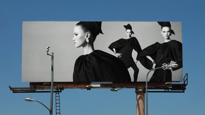 An outdoor billboard displaying a high-contrast black and white fashion advertisement against a bright blue sky.