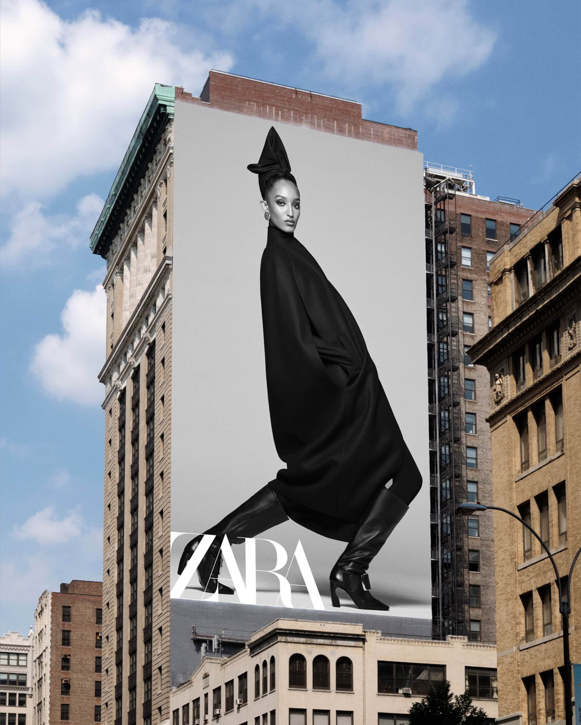 A massive Zara billboard poster on a tall urban building exterior featuring a model in a long black coat and high boots.