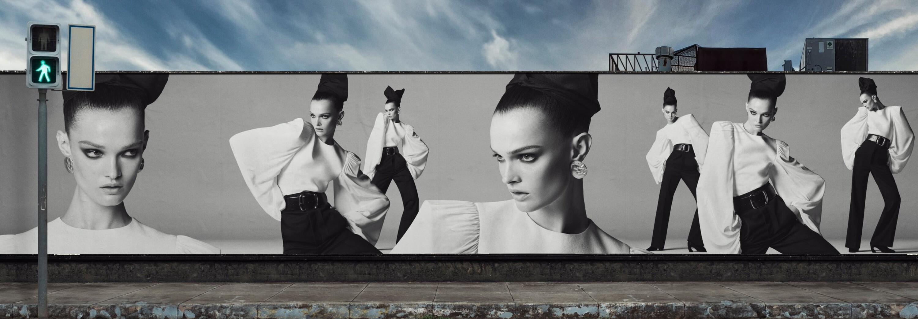 Monochrome billboard ad featuring multiple models in white blouses and black trousers under a cloudy sky.