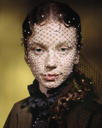 Model wearing black dotted veil with pearls over face and dark braided hair for Dior Cruise 2025 campaign