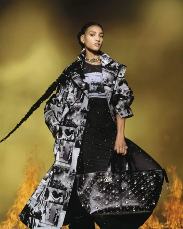 Model wearing a black and white printed coat holding a black handbag with flames flickering in the background.