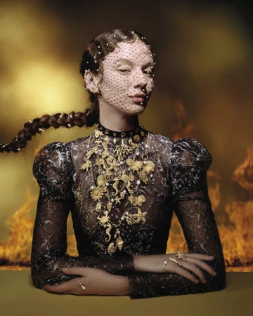 Model wearing a black lace top with ornate gold jewelry and a beaded face veil against a moody backdrop