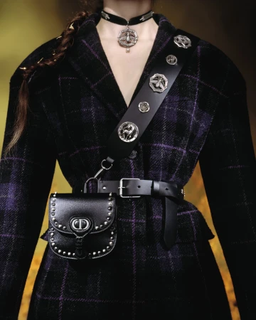 Model wearing a dark plaid jacket, black leather bag, studded strap, and choker necklace for Dior Cruise 2025 campaign.