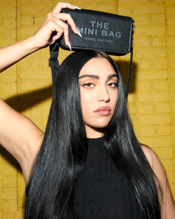 Woman holding a black leather Marc Jacobs Mini Bag above her head against a textured yellow brick wall