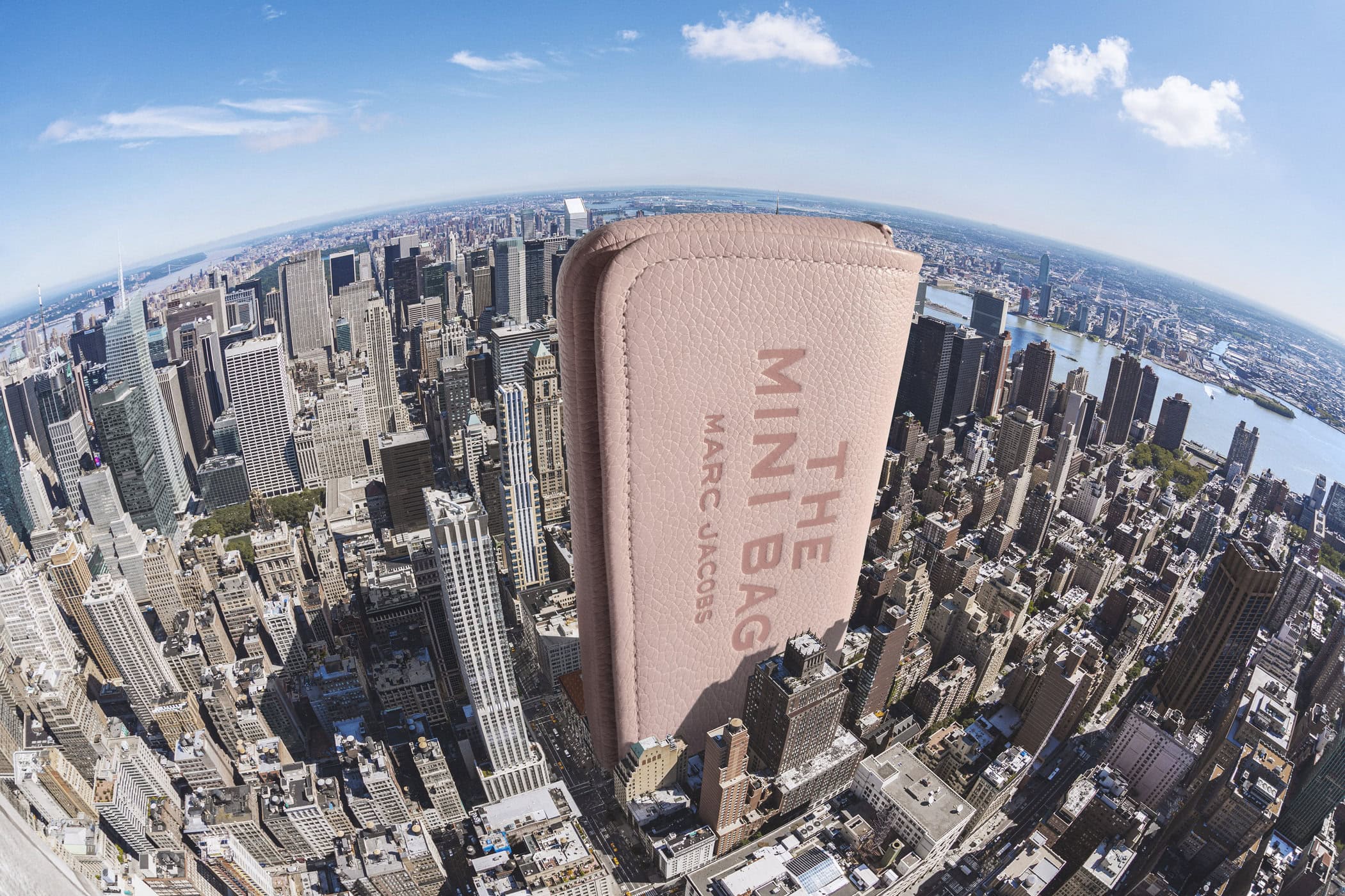 Giant pink Marc Jacobs mini bag standing upright over a sprawling aerial view of the New York City skyline