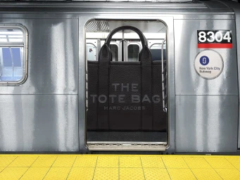 Large black leather tote bag filling the open sliding door of a silver subway train car on a platform.