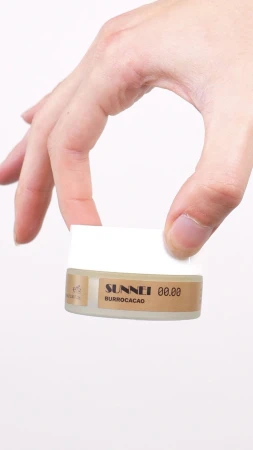 Close-up hand holding a small cosmetics jar against a plain white background