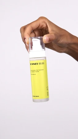 Hand holding a cylindrical yellow skincare bottle against a plain white studio background.