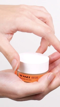 Close-up of hands opening a small round container with a white lid and an orange label against a white background.