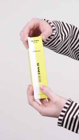 Close-up of hands opening a yellow and white product box wearing a brown and white striped long-sleeve top against a neutral background.