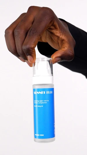 A dark-skinned hand holding a frosted skincare bottle with a bright blue label against a white background.