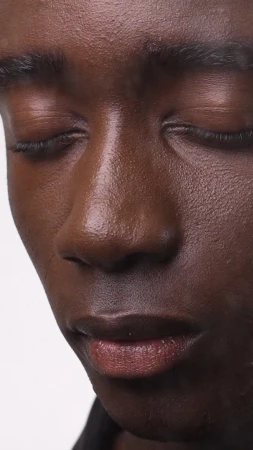 Close-up portrait of a black man with eyes closed against a neutral white background for Sunnei x midnight 0000.