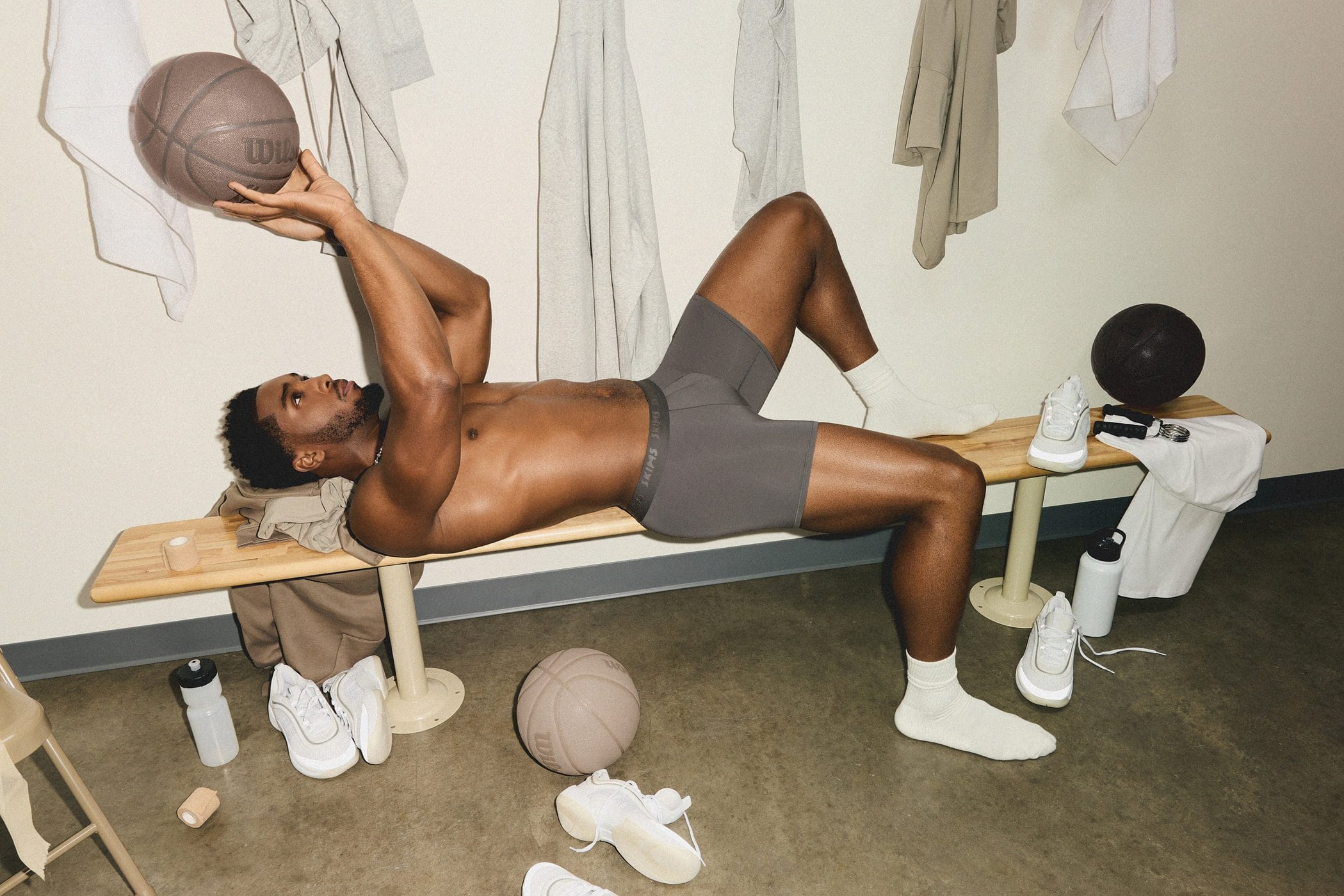 Donovan Mitchell lying on a wooden locker room bench holding a basketball for the SKIMS Fall 2024 campaign