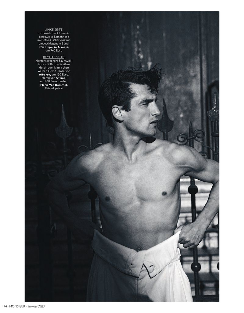 Shirtless adult male with dress pants in a photo studio with an outdoor backdrop, emphasizing fashion and male physique in black and white.