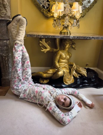 Model Loli Bahia lying on floor with legs up against wall wearing floral print loungewear and white shearling boots by Chanel
