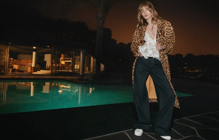 Model standing poolside at night wearing a leopard print coat and wide trousers for Zimmermann Resort 2025