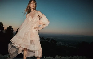 Model in a pale pink strapless ruffled dress standing outdoors against a twilight sky and distant city lights.