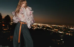Model in ruffled floral blouse and denim jeans posing against a glowing night city skyline backdrop