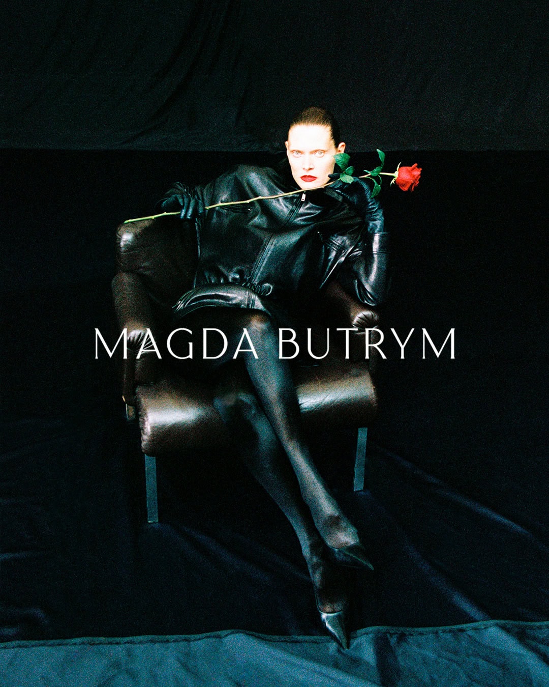 Model Malgosia Bela seated in a leather armchair holding a red rose for Magda Butrym campaign